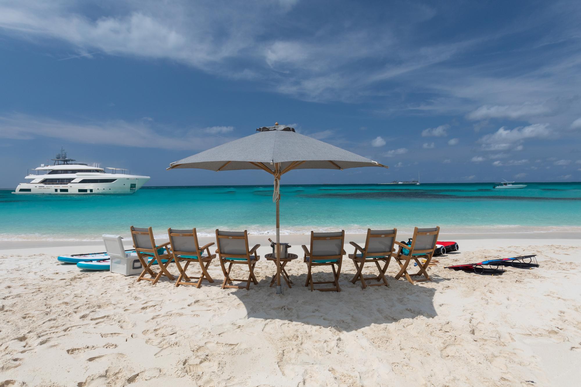A beautifully arranged beach setup beside the AMORE yacht, featuring elegant furniture and decor, creating an inviting atmosphere for a luxurious outdoor experience. | AMORE yacht, beach setup, luxury outdoor space, seaside decor | Fraser Yachts