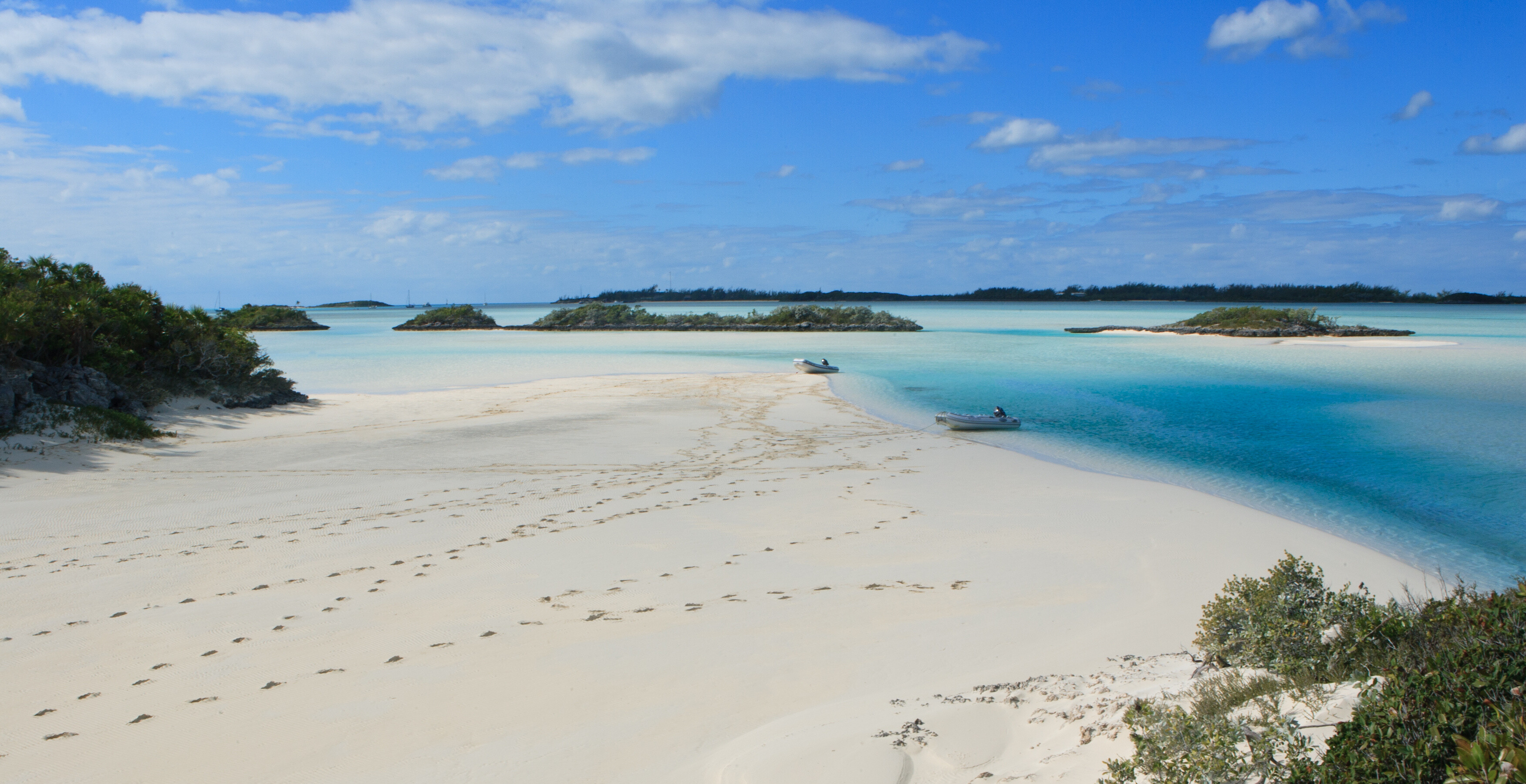 A private beach near Norman’s Cay, Bahamas—dinghies rest ashore beside fresh footprints in the sand, offering a peaceful landing spot for yacht guests in the Exumas | Fraser Yachts