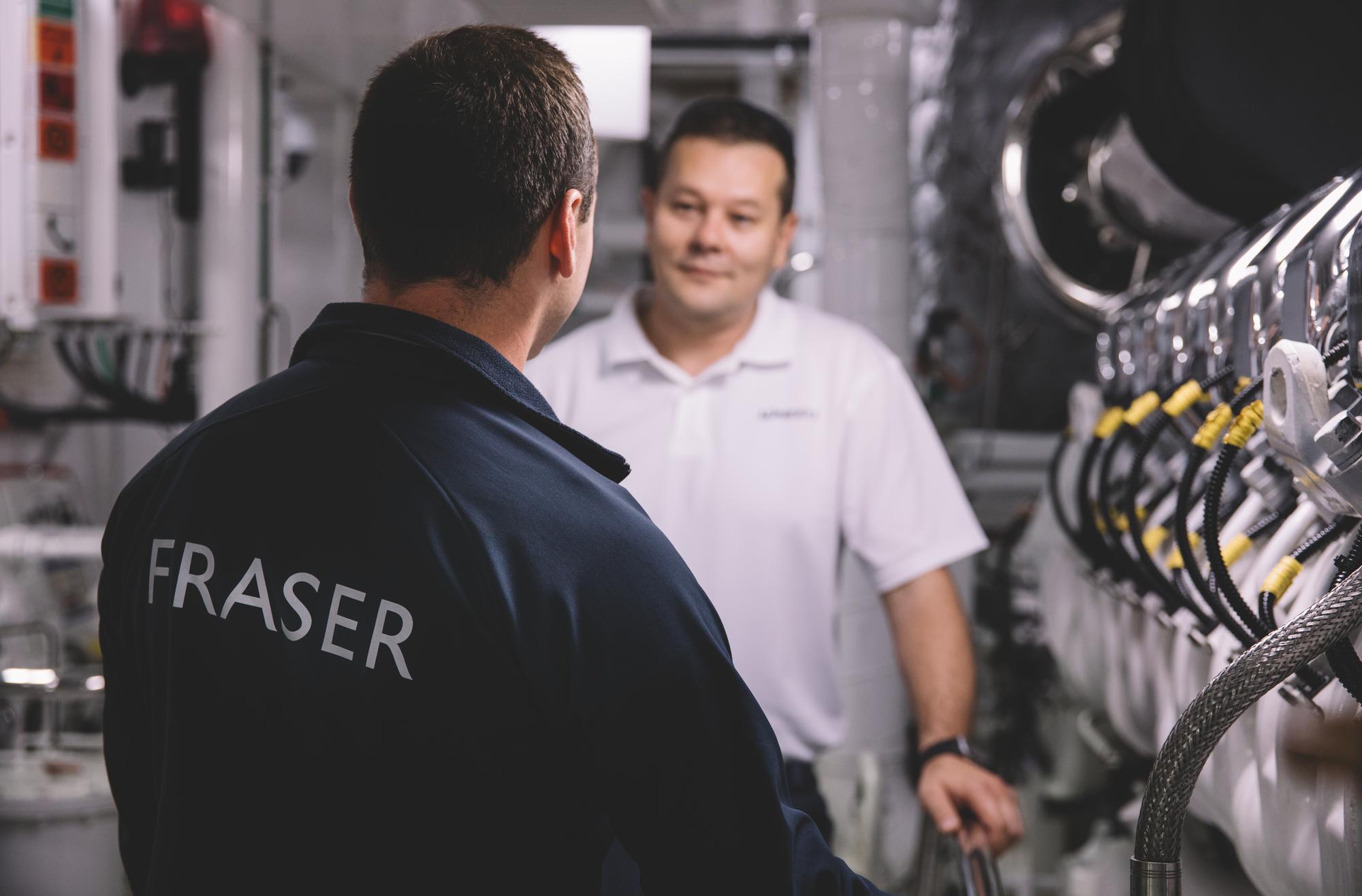 Two crew members from Fraser Yachts discussing yacht maintenance while surrounded by equipment and tools, emphasizing teamwork and professionalism. | yacht crew, yacht maintenance, Fraser Yachts logo, teamwork | Fraser Yachts