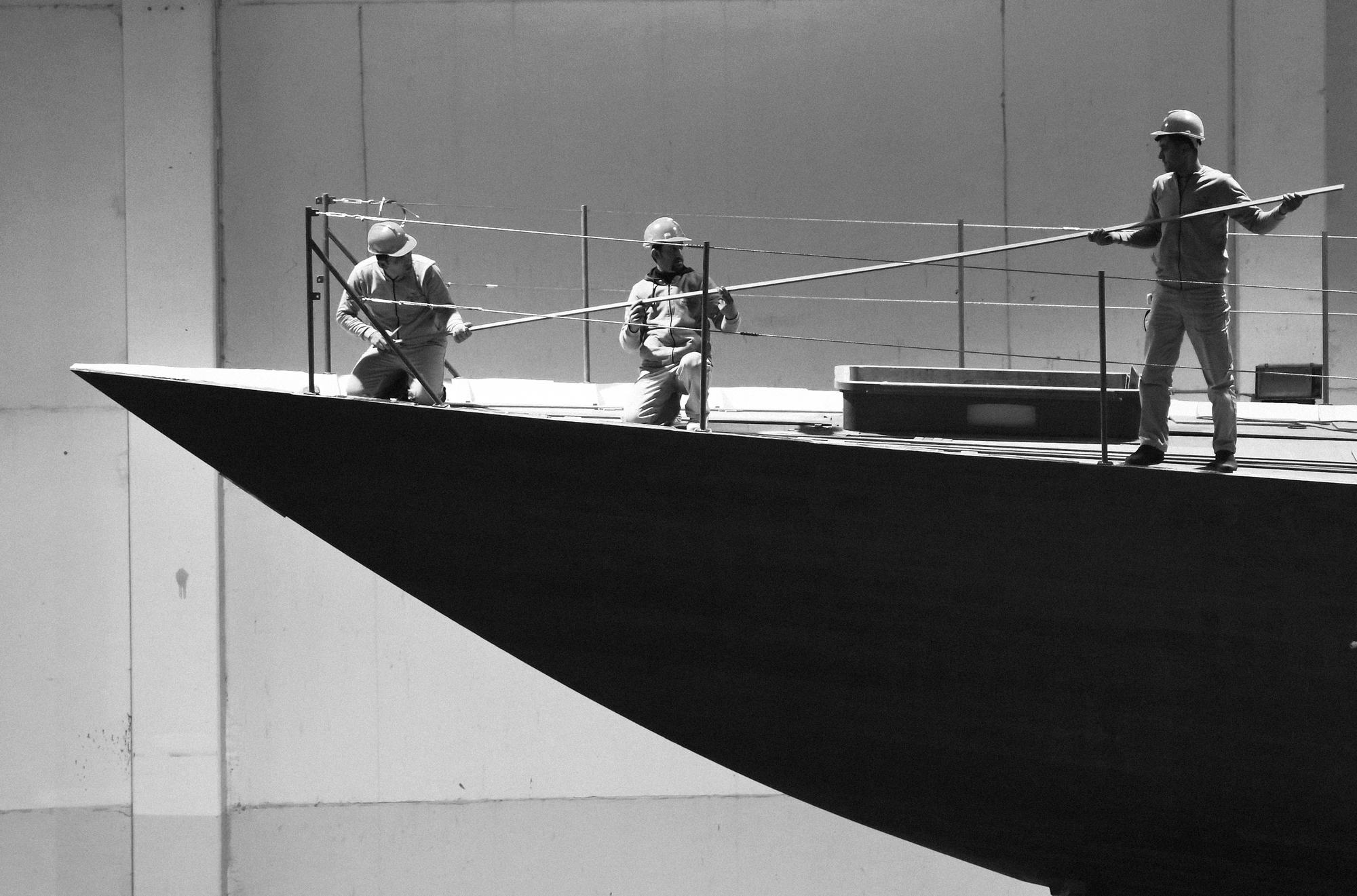 Three workers on the bow of a yacht, collaborating during the construction process at Ameller Build. | yacht construction, boat building, Ameller Build, yacht bow | Fraser Yachts