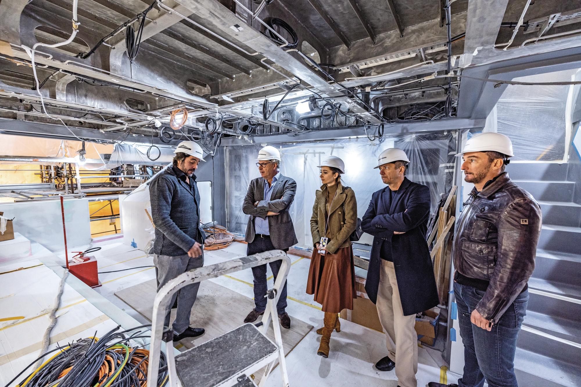 A group of professionals collaborating at a yacht construction site, discussing project details and overseeing the build process. | yacht construction, project management, teamwork, yacht building | Fraser Yachts