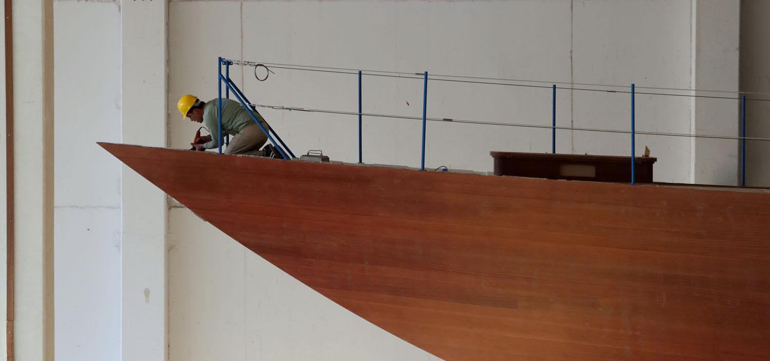 A worker standing on the bow of a yacht during the construction process, focusing on details to ensure high-quality craftsmanship. | yacht construction, boat building, worker on yacht, bow of yacht | Fraser Yachts