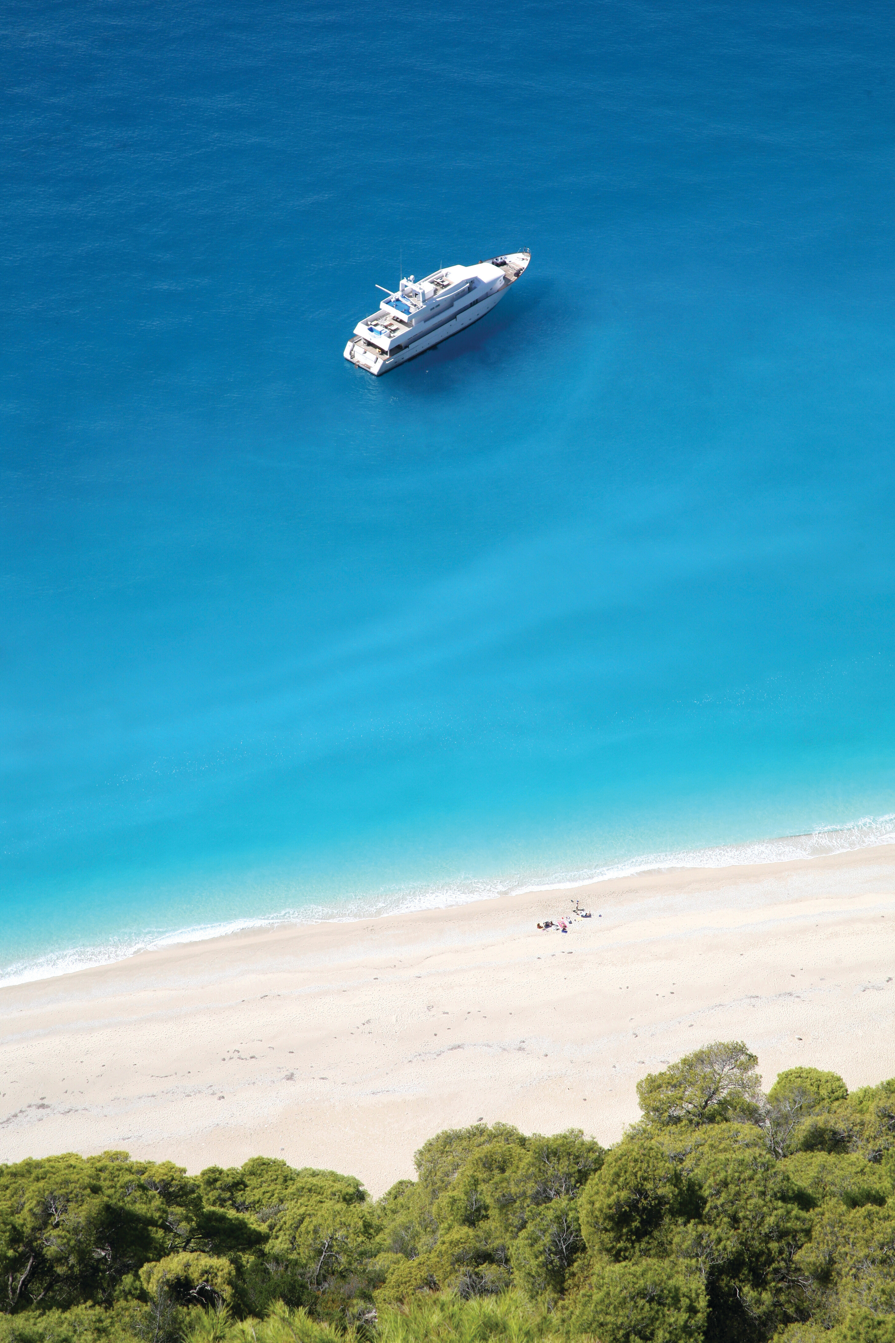 Pristine beach in Greece with a yacht offshore—turquoise waters and sandy shores create an ideal Mediterranean setting for luxury cruising and secluded anchorages | Fraser Yachts