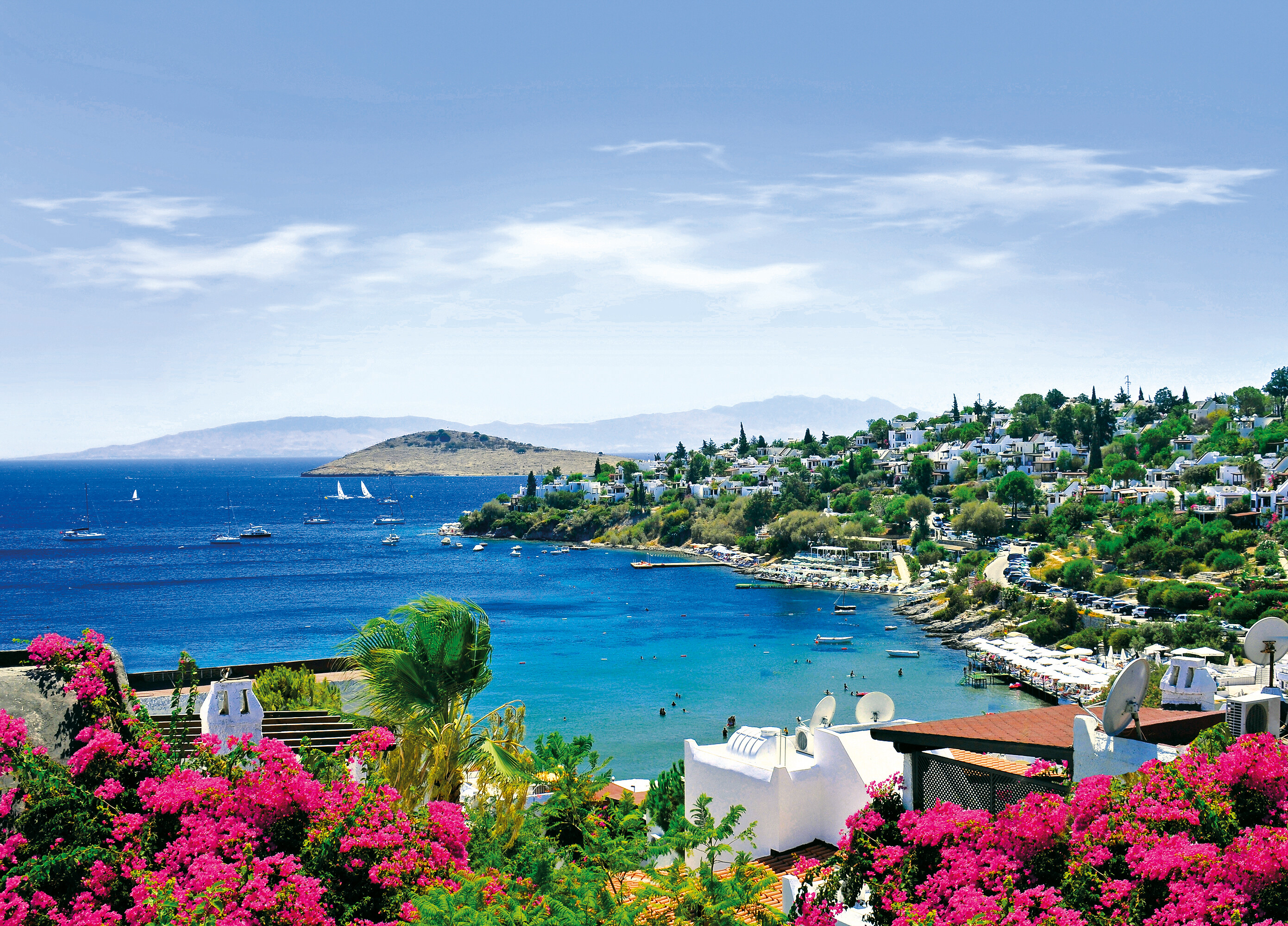 Scenic coastal view of Yalıkavak, Bodrum, Turkey, featuring whitewashed houses, vibrant bougainvillea, and turquoise Aegean waters with sailing boats.