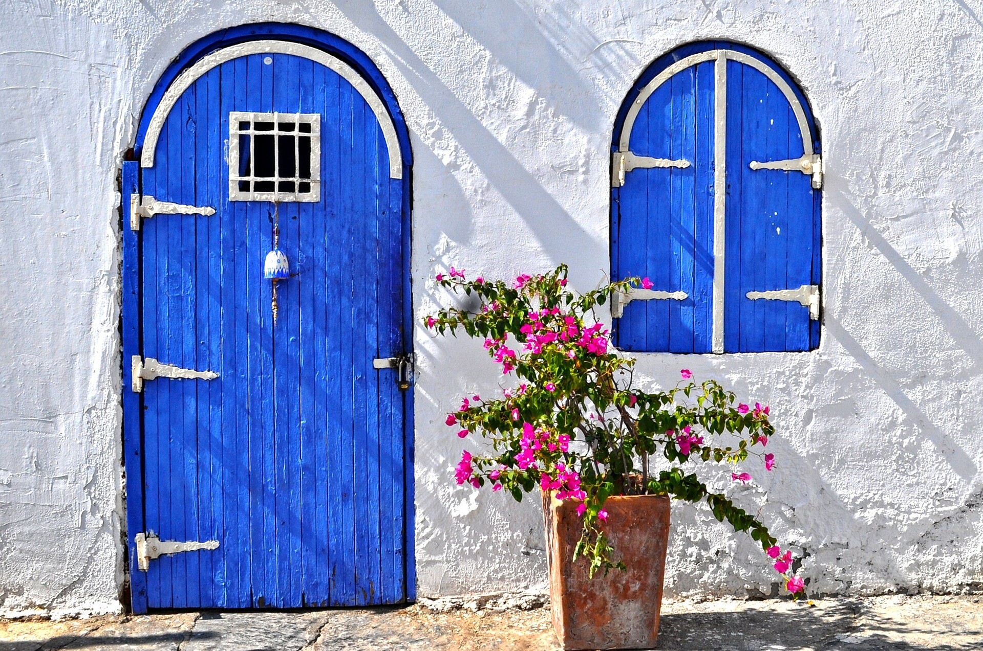 Traditional blue wooden door and window on a whitewashed house in Bodrum, Turkey, with vibrant pink bougainvillea in a terracotta pot