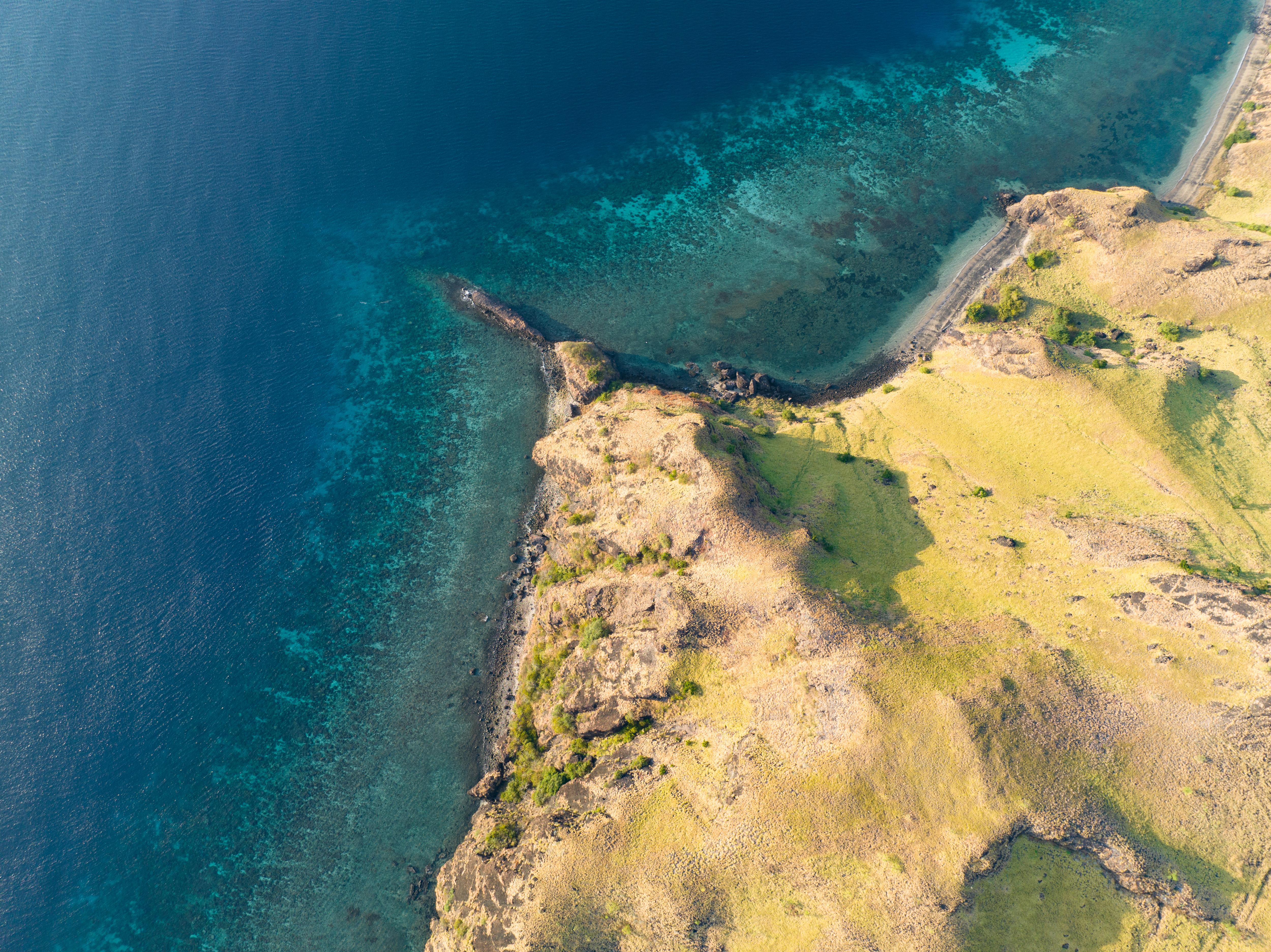 Aerial view of Rinca Island, Komodo National Park, Indonesia—where golden headlands meet vibrant coral reefs, perfect for trekking, snorkeling, and remote beach landings | Fraser