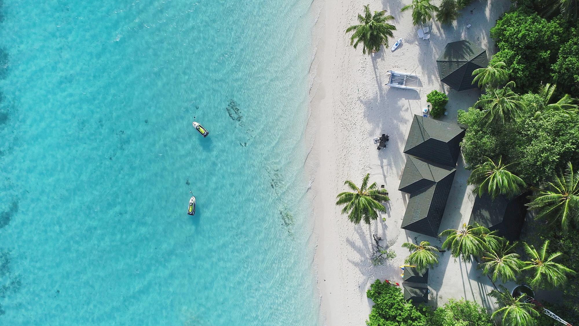 Soak in the beauty of the Maldives from above, featuring a stunning tropical beach, white sand, jetskis, and luxury bungalows. | Aerial, Beach, Beautiful, Sand, Tropical, Jetski, Bungalow | Fraser