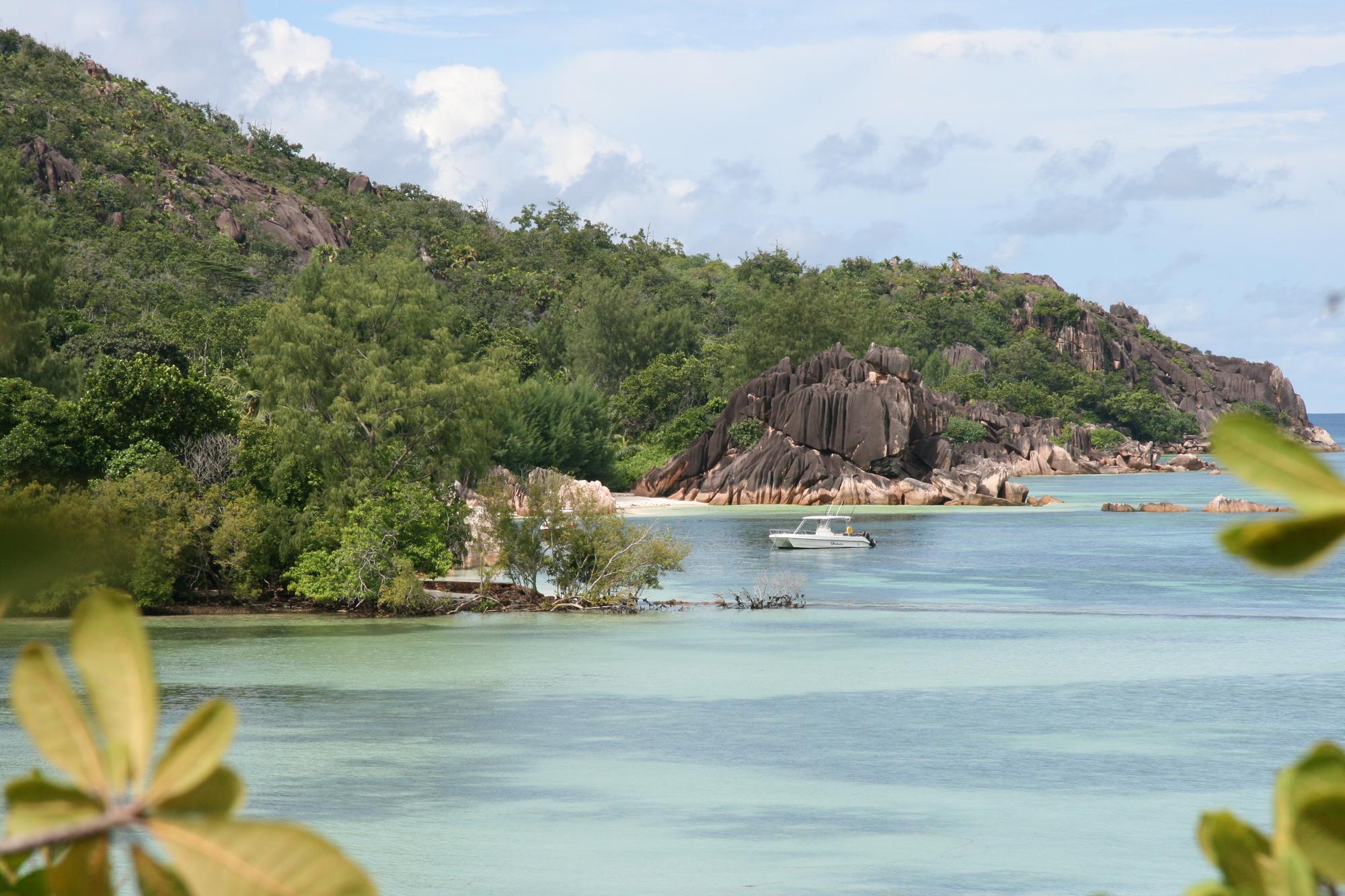 Explore Cousin Island in Seychelles with its beautiful beach, boats, lush trees, and striking rock formations in turquoise waters. | Beach, Boat, Trees, Rock Formations, Turquoise Water, Seychelles | Fraser